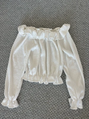 Vit offshoulder blus med volang - Supersöt vit offshoulder blus med volangkant upptill och vid ärmslut. Perfekt att styla med jeans eller kjol för en trendig look 🍒🤍Använd 1 gång!