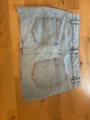 Ljusblå jeanskjol från Kappahl - Trendig ljusblå jeanskjol från Kappahl med rå kant nertill och klassiska fem fickor. Kjolen har bälteshällor och knappstängning framtill. Perfekt för dig som gillar en avslappnad och cool stil.