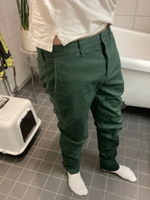 Mörkgröna chinos från Lacoste  - Säljer ett par mörkgröna chinos från lacost med klassisk rak passform och diskreta fickor både fram och bak. Byxorna har en liten lacost-logga ovanför ena bakfickan och är tillverkade i ett mjukt bomullsmaterial. Perfekta för en clean och avslappnad stil.