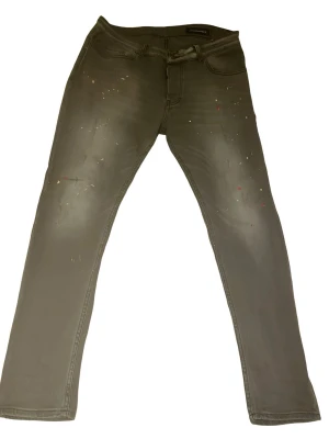 Grå jeans med färgstänk Dsquared2 - Snygga grå jeans från Dsquared2 (34/32) med raka ben och coola färgstänk över hela framsidan. Klassisk femficksmodell och diskret logga bak i linningen. Jeansen har en modern passform och är tillverkade i ett mjukt bomullsmaterial med stretch.