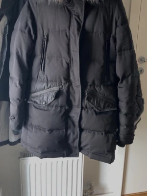 Rockandblue vinterjacka  - Snygg svart parkas med fuskpäls på huvan och quiltad design. Jackan har två stora fickor med lock och knappar samt två bröstfickor med dragkedja. Perfekt för kalla dagar och har en klassisk, rak passform.