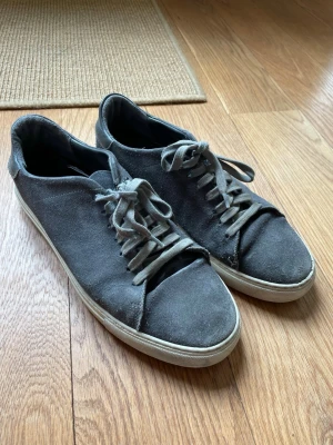 Grå mockasneakers från Axel Arigato  - Stilrena sneakers i grå mocka med matchande grå skosnören och vita gummisulor. Klassisk låg modell som passar till det mesta. Skorna har en enkel och clean design utan synliga loggor eller detaljer. Sulan saknas
