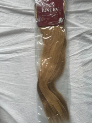 Blont löshår från Luxury - Säljer ett paket blont/brunt löshår från Luxury, gjort av 100% äkta människohår. Håret är långt, rakt med en lätt våg och kommer i en försluten plastförpackning. Perfekt för dig som vill ha extra volym eller längd! Det är många clips i satta och håret är jätte lent och fint! Jag har använt löshåret 2 kvällar ungefär sen bestämde ja mig för att bli väldigt blond..😆