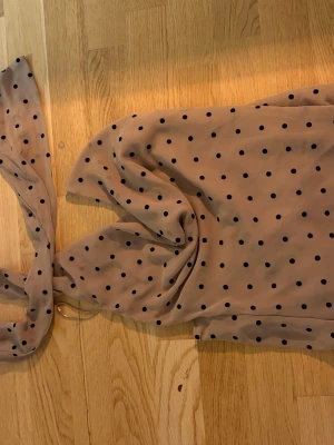 Beige sjal med svarta prickar - Säljer en beige sjal med svarta prickar. Sjalen är tunn och luftig, perfekt att slänga över axlarna. Materialet känns mjukt och lätt, och den har en klassisk rektangulär form. Prickigt mönster ger en cool retrovibe.