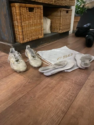 Adidas F50 elite vita fotbollsskor stl 41 1/2 - Säljer ett par vita Adidas F50 fotbollsskor. I okej skick lite trasig i vänster sko vid hälen. Får med två sulor till varje sko (4 totalt). Du får med en påse också. Skokartong saknas 