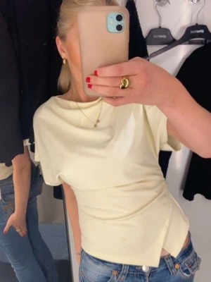 Gul topp från Gina - Snygg gul topp med omlott-detalj i midjan och korta ärmar. Toppens mjuka material och asymmetriska nederkant ger en cool och modern vibe💞💞💞