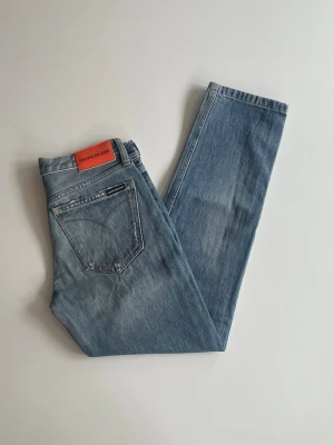 Ljusblå raka jeans Calvin Klein - Säljer ett par ljusblå raka jeans från Calvin Klein Jeans. Klassisk femficksmodell med låg midja och snyggt läderpatch bak. Jeansen är i mjuk denim och har en avslappnad passform som passar perfekt till vardagslooken. W25/L32