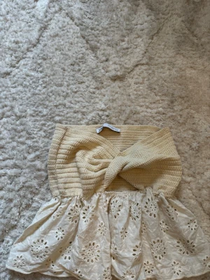 Beige virkad bandeau topp med spets - Supersöt bandeau topp i beige med virkad överdel och volangig spets nedtill. Toppen är axelbandslös och har ett twistat parti framtill. Perfekt för sommarens alla tillfällen!