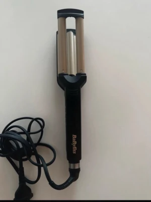 BaByliss vågtång svart och silver - Säljer en vågtång från BaByliss i svart och silver. Tången har dubbla cylindrar i metall och ett ergonomiskt handtag med tydlig logga. Perfekt för att skapa snygga vågor i håret. Sladd medföljer och värmereglering finns på sidan.