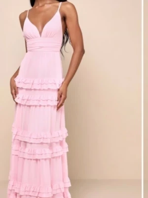 Ljusrosa långklänning med volanger Lulus strl.L(40) - Superfin ljusrosa långklänning med smala axelband och flera lager volanger från Lulu’s. Klänningen har v-ringning och är perfekt för sommarens baler. Materialet känns lätt och flowy, vilket ger en romantisk vibe. Strl.L(40) Nyskick