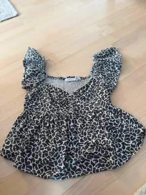Leopardmönstrad topp med puffärm - Säljer en leopardmönstrad topp från High Soy i storlek S. Toppen har v-ringning, puffiga korta ärmar och smockad rygg. Materialet är 50% rayon och 50% bomull vilket gör den mjuk och luftig. Perfekt för dig som vill sticka ut lite extra.