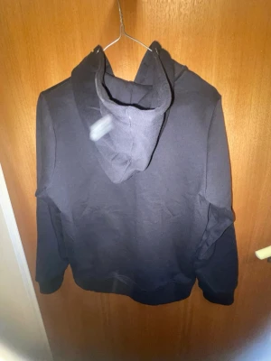 Svart zip-hoodie med fickor - En stilren svart hoodie med dragkedja framtill och två fickor. Klassisk modell med huva och ribbade muddar vid ärmslut och nederkant. Perfekt för en avslappnad look. Materialet känns mjukt och bekvämt, troligtvis bomullsblandning.