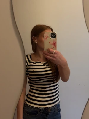 Randig topp från Tommy Hilfiger - Säljer en snygg vit och marinblå randig topp från Tommy Hilfiger. T-shirten har korta ärmar, rund halsringning och en tight passform. Storlek:176