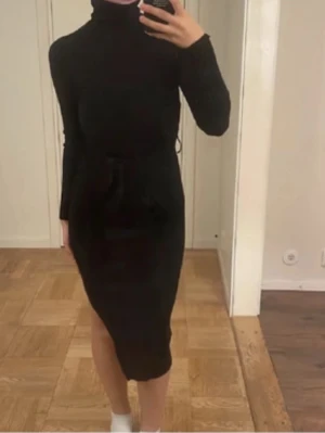 Svart långärmad poloklänning - Säljer en svart, långärmad klänning med polokrage och knyt i midjan. Klänningen har en smickrande, figurnära passform och går ner till knäna. Perfekt för dig som gillar stilrena och klassiska plagg.