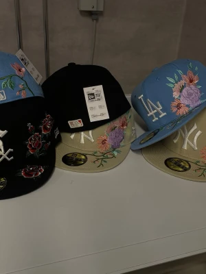 Broderade New Era kepsar med blommor (pris per Styck) - Säljer flera New Era snapbacks med broderade blommor och lagloggor som LA Dodgers, NY Yankees och Chicago White Sox. Finns i svart och ljusblått med detaljer i vitt, beige och färgglada blommor. Perfekt för dig som vill sticka ut med en unik och trendig keps. SÄLJER  PRIS PER STYCK