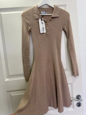 Beige ribbad klänning från Bik Bok - Supersnygg beige ribbad klänning från Lindex med krage, långa ärmar och guldknappar framtill.