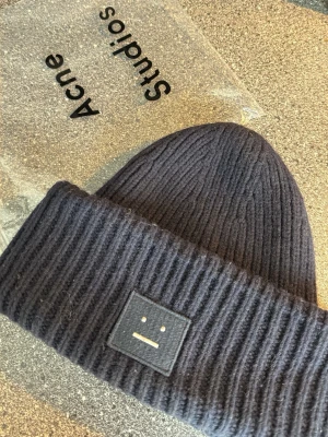  Acne Studios - Säljer en mörkblå ribbstickad mössa från Acne Studios med den ikoniska Face-loggan framtill. Mö labor i mjuk ullmix och har en bred uppvikt kant för extra stilpo scan. Perfekt accessoar för kalla dagar.