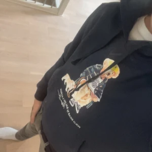 Mörkblå hoodie med tryck från Ralph Lauren - Snygg mörkblå hoodie från Ralph Lauren med ikoniskt björntryck på bröstet. Klassisk huva med dragsko och ribbade muddar. Perfekt för en avslappnad och trendig stil. Materialet känns mjukt och bekvämt mot huden. Storlek M kan passa S också. Varmt och bekvämt material. 