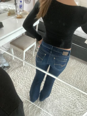 Mörkblå bootcut jeans från Replay - Säljer ett par mörkblå bootcut jeans från Replay med klassiska fem fickor och snygga slitningar. Jeansen har en figurnära passform upptill och lätt utsvängda ben. Perfekta för dig som gillar en tidlös och trendig look.