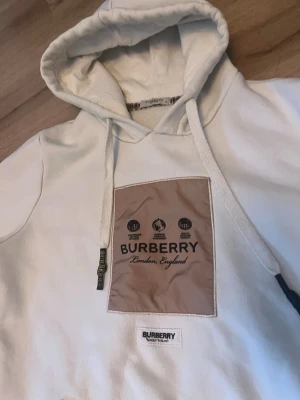  hoodie från Burberry - Snygg vit hoodie från Burberry med stor beige patch på bröstet och Burberry-logga.