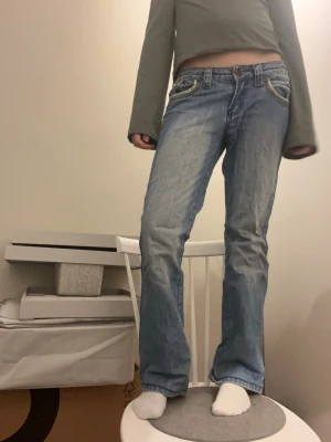 Ljusblå bootcut jeans med detaljer - Säljer ett par ljusblå bootcut jeans med slitningar och snygga sömdetaljer vid fickorna. Köpt för 400 men alldrig andvänt! Storlek S, köpt på Plick 