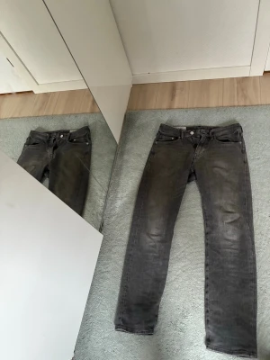 Gråa raka jeans - Säljer ett par gråa jeans med rak passform och klassisk femficksdesign. Jeansen har knappgylf och bälteshällor. Materialet är denim i bomull och färgen är något tvättad svart för en cool look. 29/32