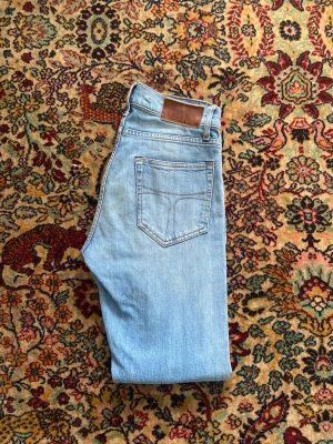 Tiger of sweden jeans - Säljer ett par klassiska ljusblå jeans från tiger of sweden med raka ben och femficksmodell. Jeansen har en brun läderpatch bak i midjan och subtila slitningar för en avslappnad look. Perfekta till vardags för en tidlös stil. W27 L30