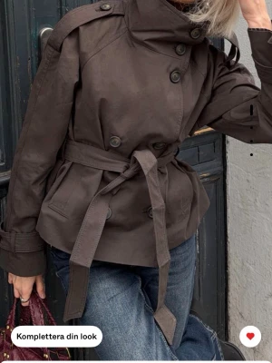 Kort brun trenchcoat med bälte - Säljer denna sjukt populära jackan från Bershka, aldrig använd med prislapp på storlek S