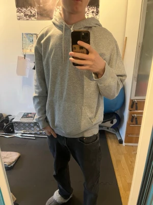 Grå basic hoodie med huva - En stilren grå hoodie med huva och dragsnören. Hoodien har en klassisk ficka framtill. Perfekt för en avslappnad och casual look. Materialet känns mjukt och bekvämt, troligen bomullsblandning.