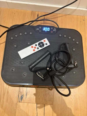 Vibrationsplatta med fjärrkontroll - Säljer en svart vibrationsplatta från Fitness Coach med digital display, fjärrkontroll och träningsband. Perfekt för hemmaträning, förbättrar balans och styrka. Plattan har halkfri yta och flera inställningar för intensitet.