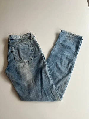 Ljusblå raka jeans - Säljer ett par ljusblå jeans med raka ben. Jeansen har slitna detaljer och en tvättad look som ger en avslappnad vibe. Perfekta för dig som gillar en enkel och stilren stil. Materialet är denim i bomull.