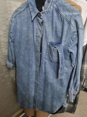 Oversized blå jeansjacka - Säljer en oversized blå jeansjacka i klassisk tvätt med en bröstficka och knäppning framtill. Jackan har nedhasade axlar och långa ärmar som kan vikas upp för en avslappnad look. Perfekt för dig som gillar vintage och streetstyle.