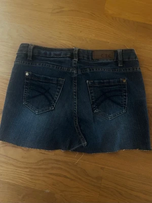 Mörkblå jeanskjol från C.I.C - Säljer en mörkblå jeanskjol från C.I.C med rå kant nertill och klassiska fem fickor. Kjolen har bälteshällor, knapp och dragkedja framtill samt bakfickor med dekorativa sömmar. Perfekt till en avslappnad stil.