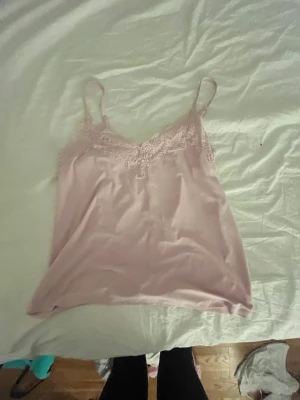 Ljusrosa spetslinne i satinlook - Supersött ljusrosa linne med tunna axelband och fina spetsdetaljer vid urringningen och ryggen. Mjukt och glansigt material som känns lyxigt mot huden..