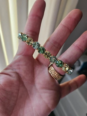 Guldarmband med gröna och gula pärlor - Snyggt armband med stora runda pärlor i grönt och gult, infattade i guldfärgad metall. Armbandet har en elastisk design som gör det enkelt att ta på och av. Perfekt accessoar för att ge din outfit lite extra färg och bling.