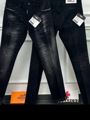 Svarta Dsquared2 jeans med slitningar - Snygga svarta jeans från Dsquared2 med coola slitningar och vita färgstänk. Jeansen har smal passform och klassisk femficksdesign. Perfekta för dig som gillar en trendig och edgy stil. pris kan diskuteras skicka ba bud