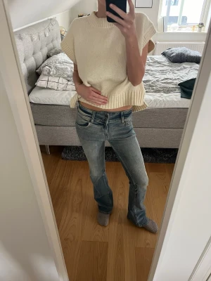 Blå bootcut jeans med slitningar - Säljer ett par blå bootcut jeans med lätt slitna detaljer och klassisk femficksdesign. Jeansen har låg midja och är tillverkade i denim med en snygg tvätt. Perfekta för dig som gillar en avslappnad och trendig look.