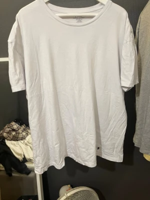 Vit t-shirt från Polo Ralph Lauren - Vit t-shirt från Polo Ralph Lauren med klassisk rund hals och diskret broderad logga i mörkblått på nedre delen. T-shirten är enkel och stilren, tillverkad i mjuk bomull och har korta ärmar. Perfekt för dig som gillar clean och tidlös stil.