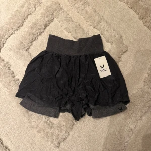 Mörkgrå shorts från SOC - Snygga mörkgrå shorts från SOC med bred resår i midjan och lös passform. Tillverkade i mjukt syntetmaterial som känns bekvämt mot huden. Perfekta för träning eller chill dagar.