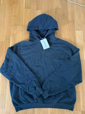 Mörkblå hoodie från Acne Studios - Snygg mörkblå hoodie från Acne Studios med stor huva och tryck på ryggen där det står 'Acne Studios STOCKHOLM 1996'. Tillverkad i mjuk bomull med ribbade muddar vid ärmslut och nederkant. Perfekt för en avslappnad och trendig look.
