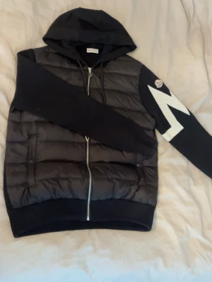 Moncler - Säljer en svart cardigan från Moncler med huva och dragkedja framtill. Jackan är ny och knappast använd. Jätte fin jacka som passar med allt. Hör av dig vid intresse!