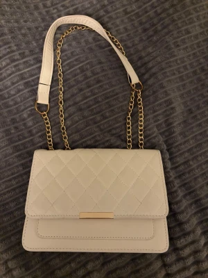 Cremefärgad axelväska  - En cremefärgad axelväska som kan både användas som hand och axelväska. Den kan kortas ner och även bli längre!