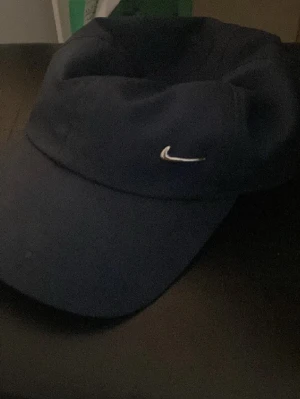 Mörkblå Nike keps med broderad logo - Snygg mörkblå keps från Nike med klassisk böjd skärm och liten vit broderad Swoosh-logo framtill. Kepsen är i mjukt tyg och har en stilren, sportig look som passar perfekt till streetwear eller träning.