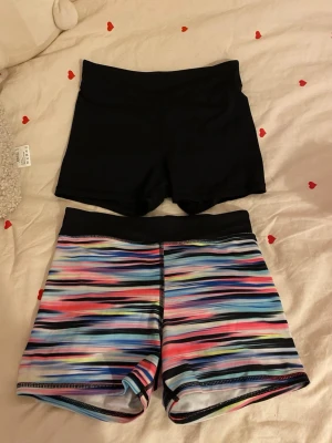 Två par sportshorts från H&M - Säljer två par sportshorts/cykelbyxor från H&M. Ett par är helsvarta och det andra har ett färgglatt randigt mönster. Silkesmaterial, skön passform och är perfekta för träning eller aktiva dagar. Storleken är 146/152 men lite stora i storleken så de passar XS mer. Säljer då jag rensar garderoben! 