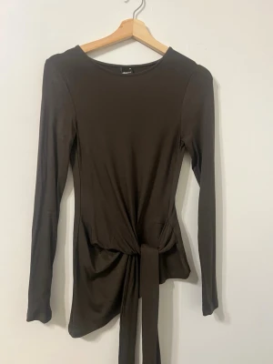 Grön långärmad topp med knyt - Grön långärmad topp med rund hals och snygg knyt-detalj i midjan. Toppen har en slim passform och är tillverkad i ett mjukt, stretchigt material som sitter skönt på kroppen. Från Gina tricot , använd en gång 