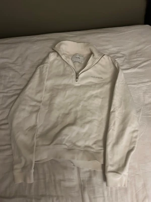 Vit half-zip sweatshirt Axel Arigato - Säljer en stilren vit sweatshirt från Axel Arigato med halv dragkedja och broderad logga på bröstet. Tröjan har hög krage och ribbade muddar vid ärmslut och nederkant. Perfekt för en clean och avslappnad look.