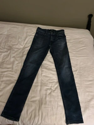 Mörkblå slim jeans från replay - Säljer ett par mörkblå replay hyperflex jeans med raka ben och klassisk femficksmodell. Jeansen har subtila slitningar framtill och är tillverkade i denim med lätt stretch. Perfekta för dig som gillar en enkel och tidlös look. Jeansen är stolek 12y men passar dig mellan 160-165 bäst