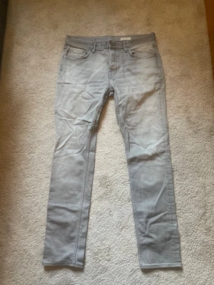 Grå jeans från AllSaints - Snygga grå jeans från AllSaints i modellen Rex. Jeansen har en smal passform, klassisk femficksdesign och är tillverkade i ett mjukt denimtyg. Perfekta för dig som gillar en stilren och modern look.