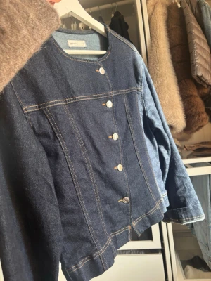 Mörkblå jeansjacka från Perfect Jeans - Snygg mörkblå jeansjacka från Perfect Jeans med rund halsringning och raka sömmar. Jackan har silverfärgade knappar framtill och klassiska kontrastsömmar. Enkel och stilren modell utan krage, perfekt för en trendig look.