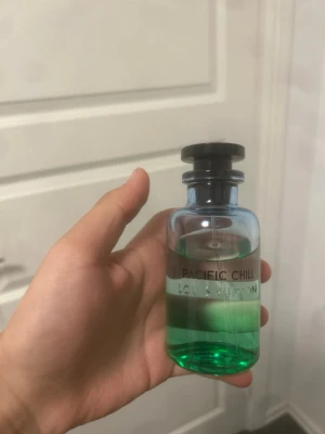 Louis Vuitton Pacific Chill parfym - Fräsch parfym från Louis Vuitton i doften Pacific Chill. Flaskan är genomskinlig med en snygg grön vätska och svart lock. Glasflaskan har en modern och stilren design med tydlig logga och text på framsidan. Perfekt för dig som gillar exklusiva dofter.